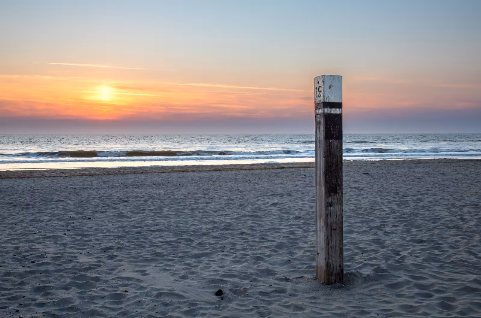 Houten paal op strand bij zonsondergang