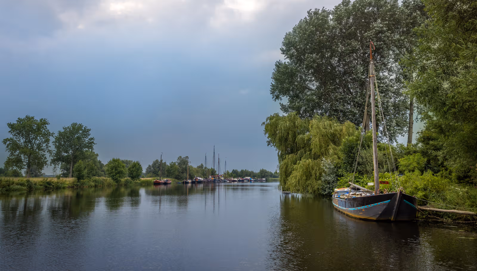 Aangemeerde zeilschepen bij groene oever