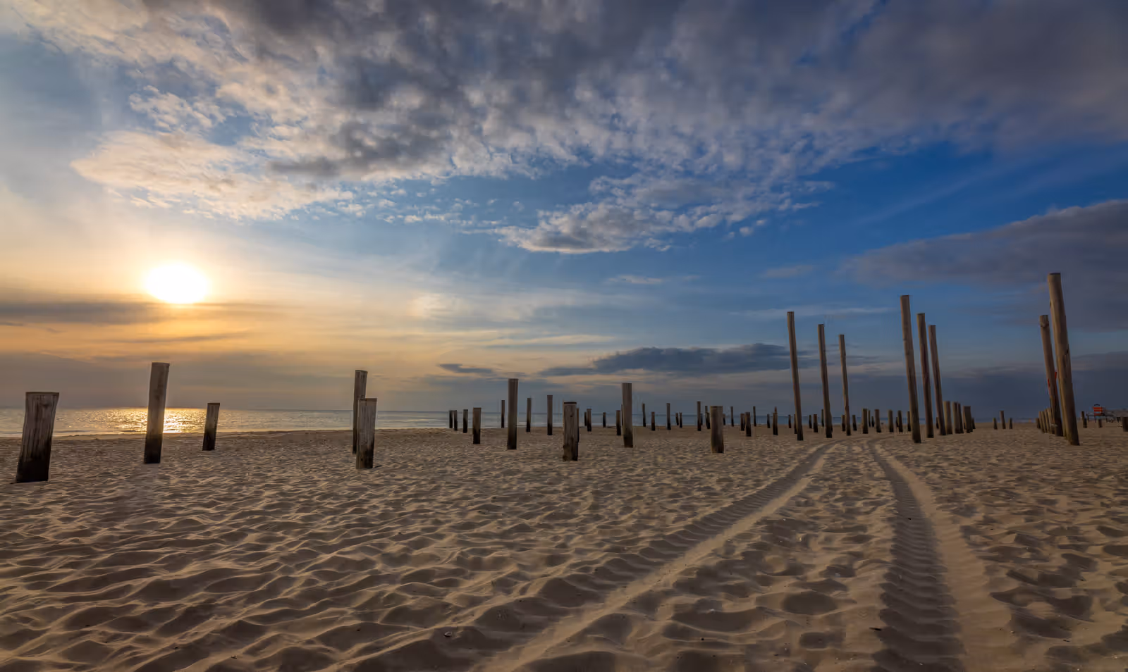 Strand met houten palen en lage zon